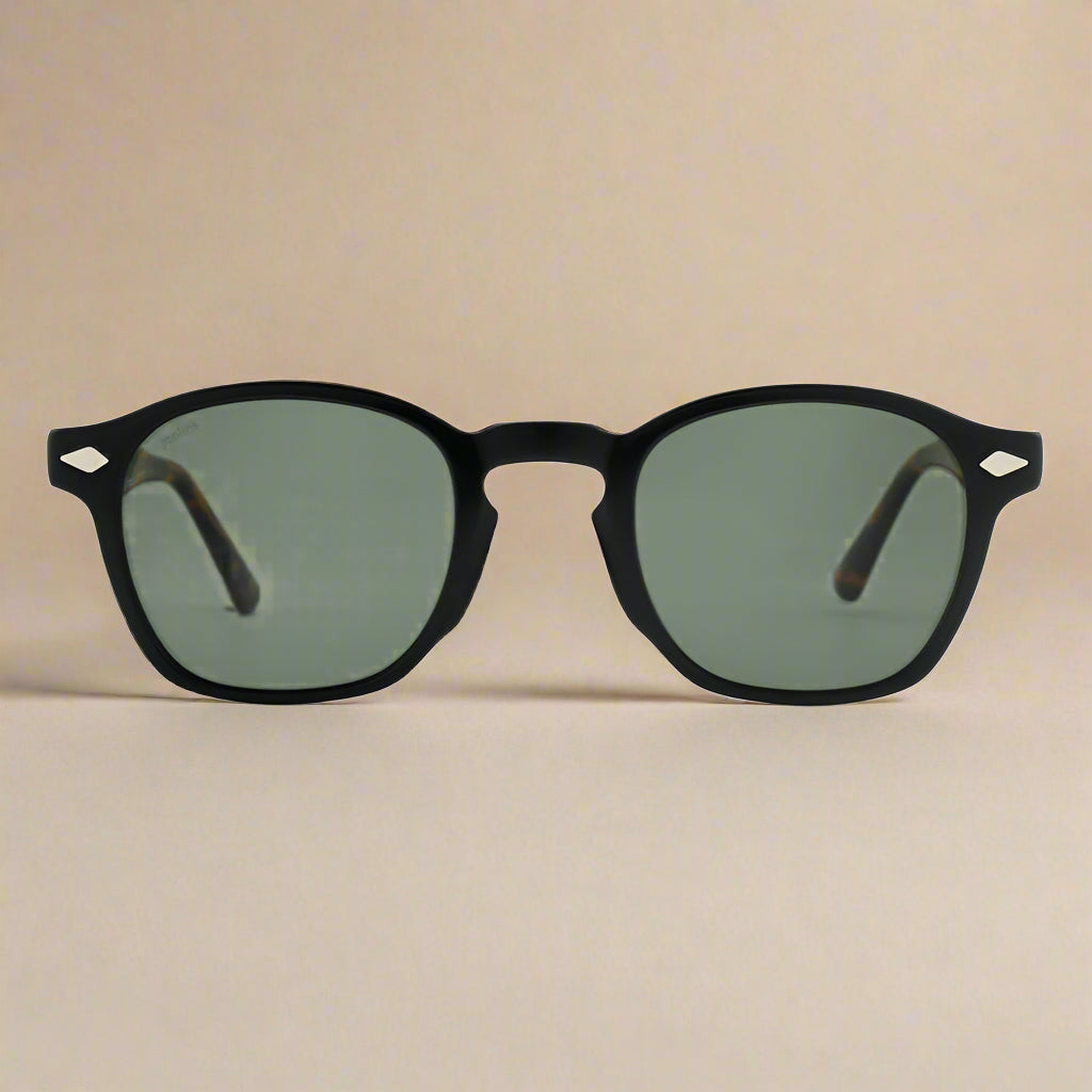 Black-framed sunglasses with green lenses on a beige background
